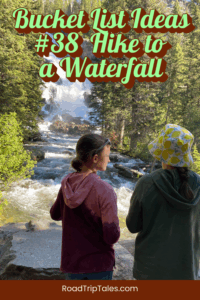 Two children stand on a forest trail overlooking a rushing waterfall surrounded by trees, featured in a summer bucket list activity.
